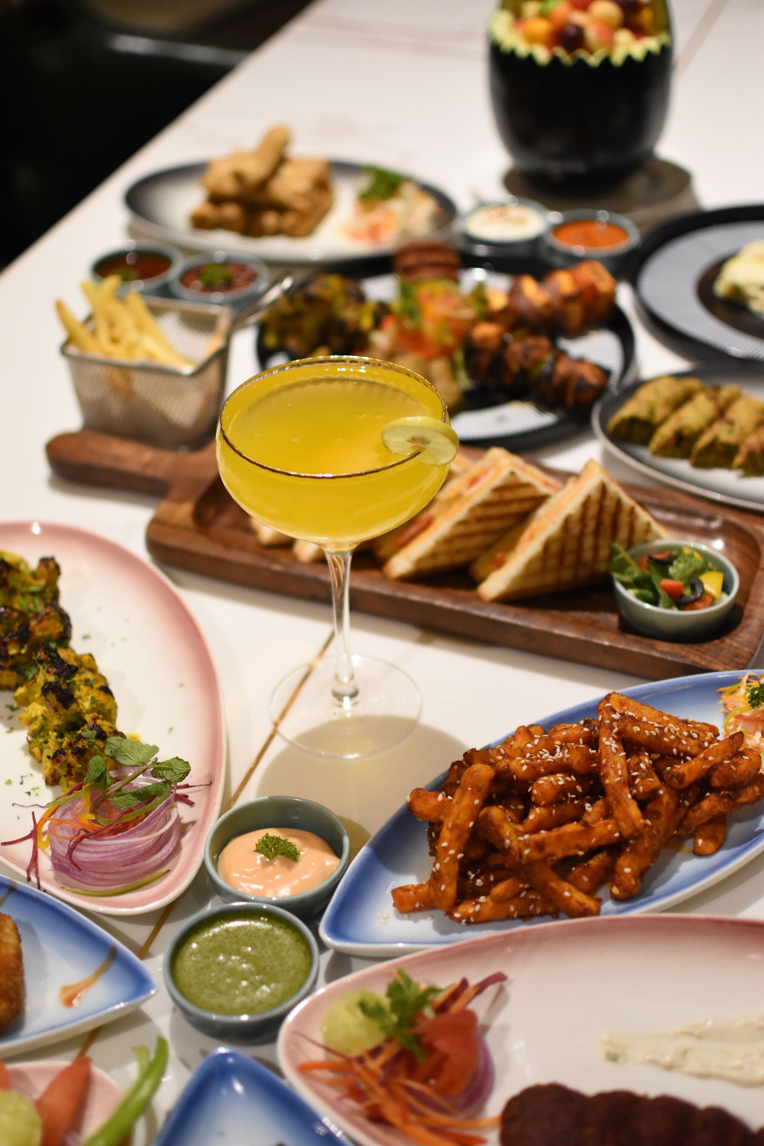 Une variété de plats, notamment des brochettes grillées, du poulet frit et des sandwichs, sont disposés sur une table.