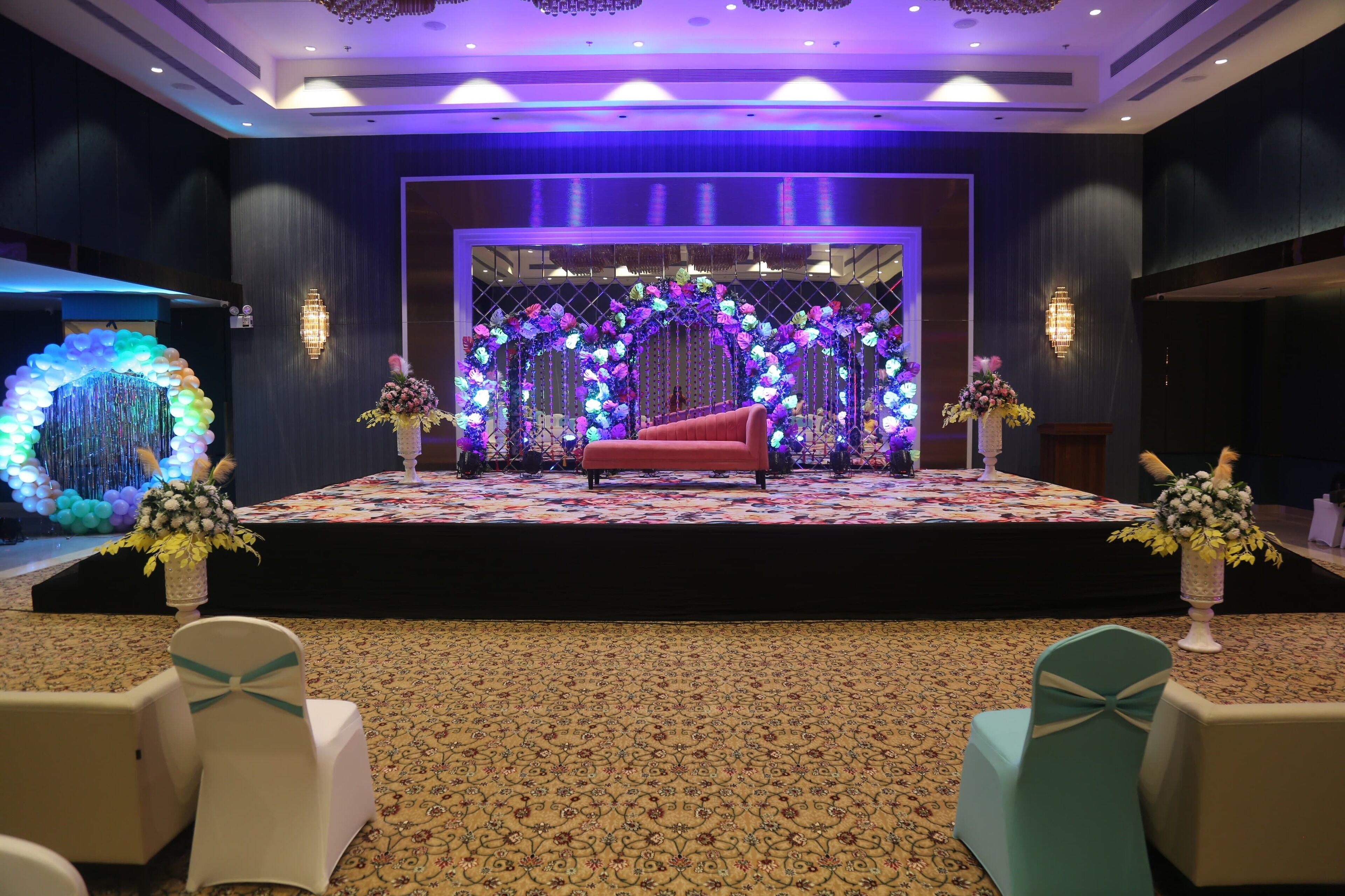 A stage with a red sofa, floral decorations, and a patterned carpet.