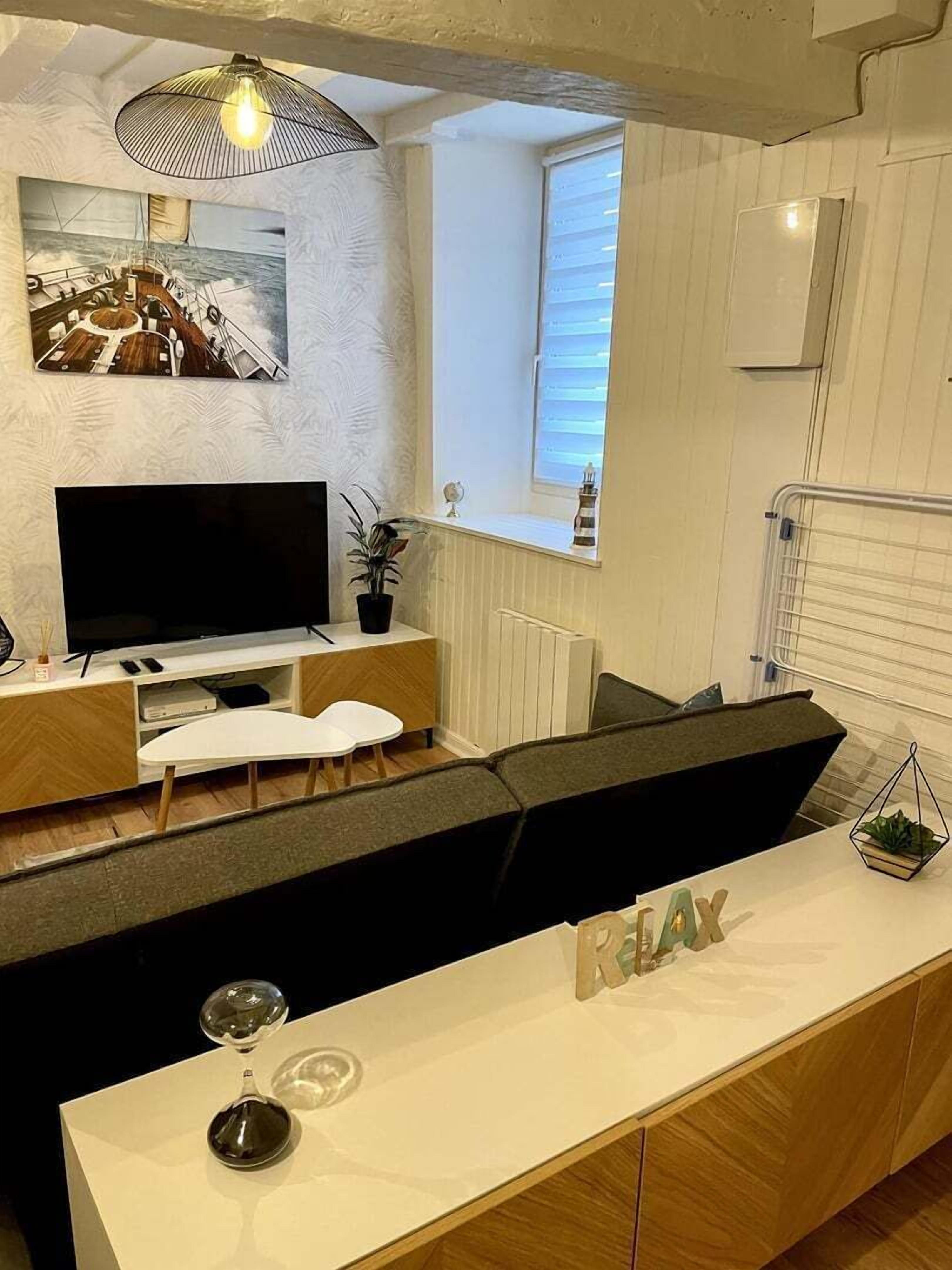 A modern living room with a flat-screen TV, a white sofa, a coffee table, and a small plant.
