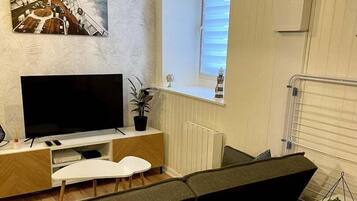 A modern living room with a flat-screen TV, a white sofa, a coffee table, and a small plant.