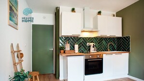 Une cuisine compacte avec des meubles blancs, un crédence vert à motifs en chevrons, une machine à café et un évier.