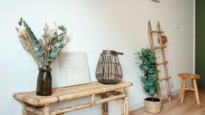 Un banc en osier, agrémenté d’un vase de fleurs séchées et d’une affiche encadrée accrochée au mur.