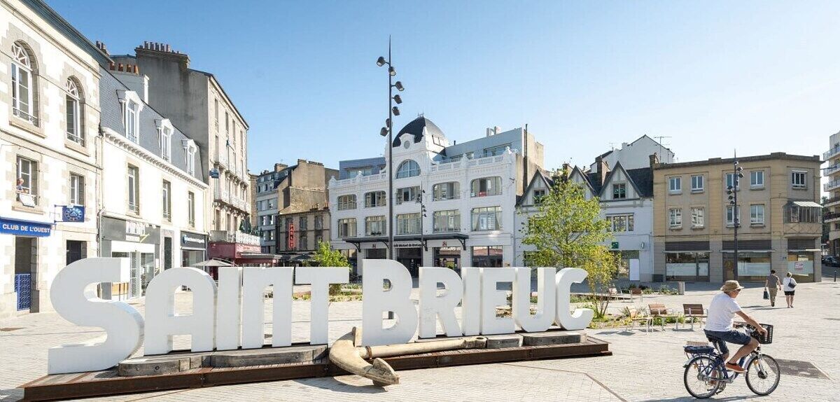 Un senyal amb la lletra "SAINT BRIEUC" en una plaça pública, amb edificis al fons.