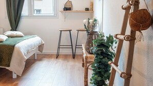 Une chambre confortable avec un lit, deux tabourets, une plante suspendue et une échelle appuyée contre le mur.