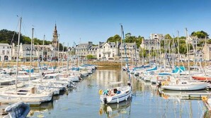 Un port de plaisance où sont amarrés de nombreux bateaux, une tour imposante en arrière-plan et des bâtiments le long de la promenade.