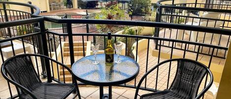 A balcony with a round table and two chairs, a bottle, and two wine glasses.