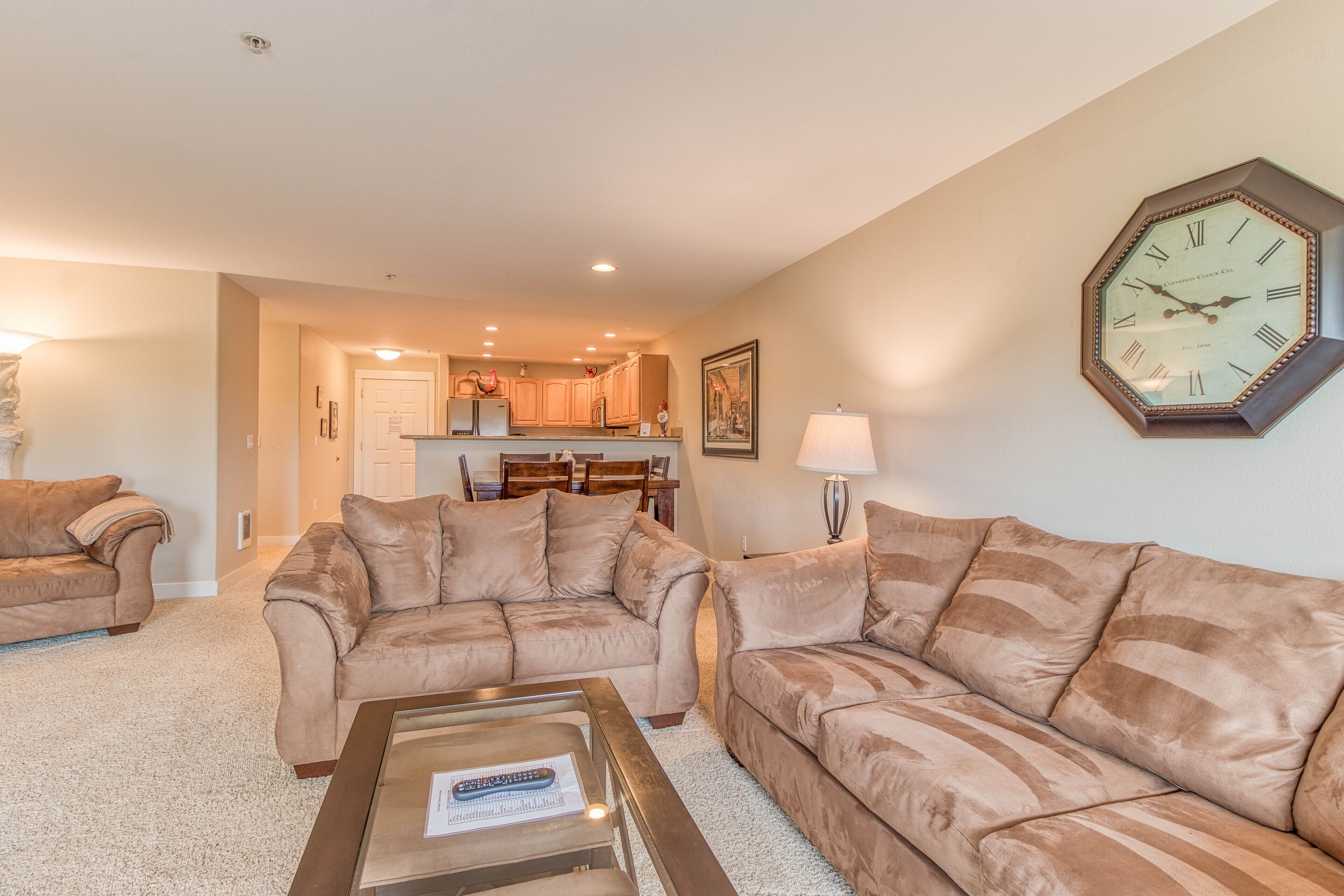 A living room with beige sofas, a coffee table, and a large wall clock.