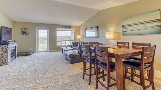 A spacious living area with a fireplace, a dining table with chairs, a sofa, and a large window.