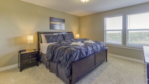 A bedroom with a bed, nightstand, lamp, and a painting on the wall.