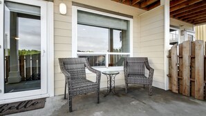 Une terrasse extérieure avec des chaises en osier et une petite table, une porte-fenêtre coulissante et une clôture en bois.