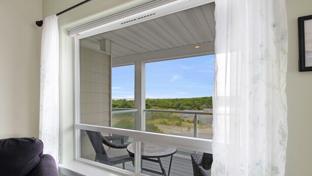 Ein Balkon mit Tisch und Stühlen, Blick ins Freie und ein Fenster mit Vorhang.