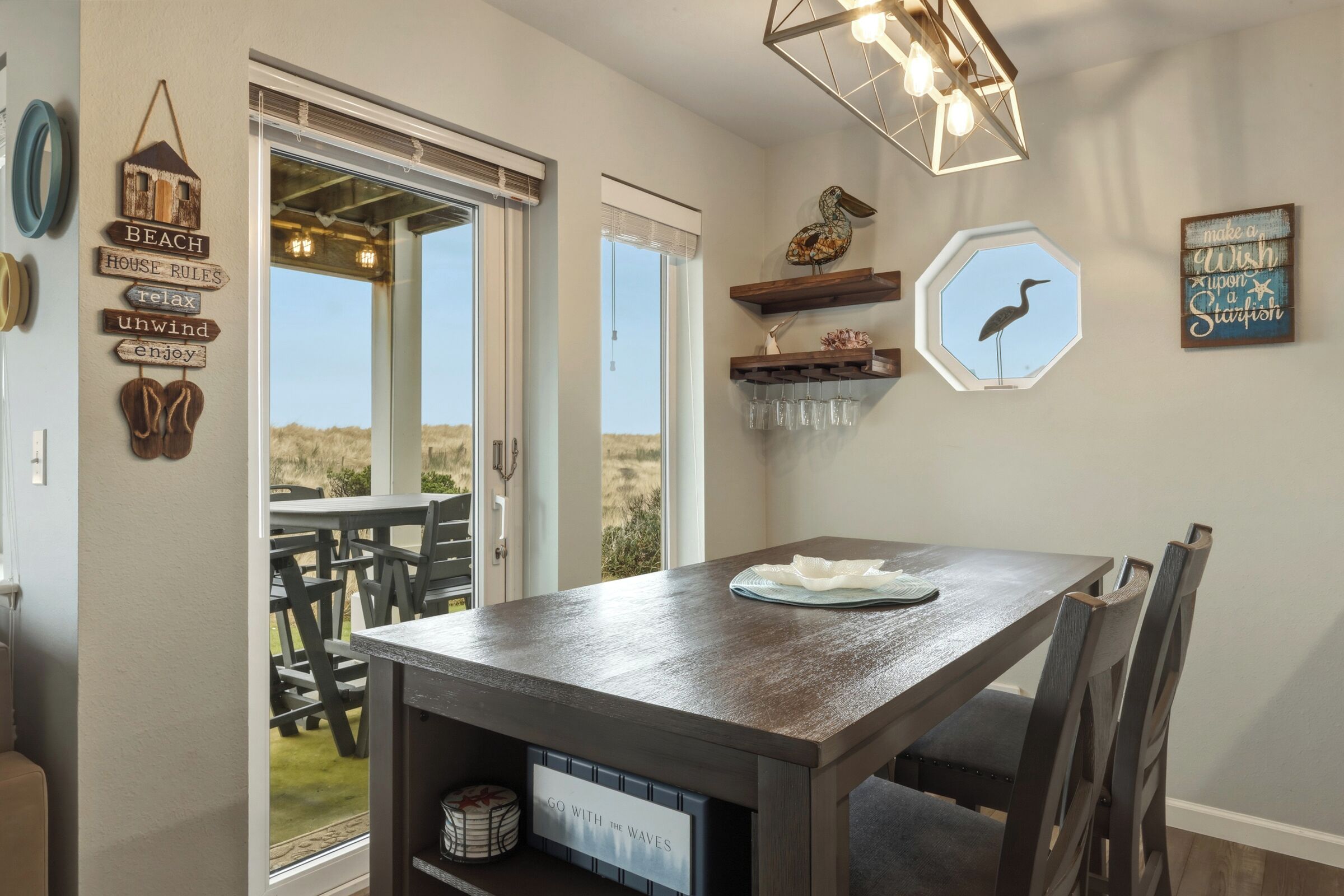 Un espace repas comprenant une table et des chaises, un luminaire suspendu et des éléments de décoration murale, notamment un oiseau et un panneau avec un message.