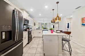 Une cuisine moderne dotée d’un îlot central, d’appareils électroménagers en acier inoxydable et de luminaires suspendus.