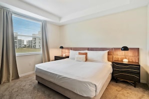 Une chambre d’hôtel avec un grand lit, deux tables de chevet, une petite table et une fenêtre avec des rideaux.