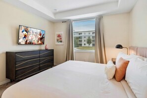 Una camera d'albergo con un letto grande, una televisione a parete, un comò e una finestra con tende.