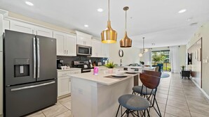 A modern kitchen with a central island, stainless steel appliances, pendant lighting, and a view to the outdoors. - Minutes From Theme Parks! Free Water Park access! (Kissimmee)