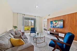 Un salon moderne comprenant un canapé, un fauteuil, une table basse et un téléviseur à écran plat fixé à un mur en bois.