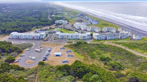 Vue aérienne d’un quartier résidentiel situé sur la côte, avec plusieurs immeubles d’appartements, un parking et une plage en arrière-plan.