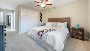 Une chambre à coucher comprenant un lit, un ventilateur de plafond, une table de chevet et une commode.