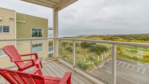Un balcon avec des chaises rouges, une vue sur l’océan et un immeuble à la façade en briques.