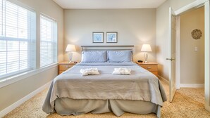 Une chambre à coucher avec un lit, deux lampes de chevet, une table de chevet, une porte et deux tableaux encadrés au mur.