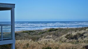 Une vue sur l’océan, avec les vagues qui déferlent, prise depuis un point de vue élevé, surplombant une zone herbeuse à la végétation clairsemée.