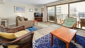 Un salon avec un canapé, des fauteuils, un téléviseur et un balcon offrant une vue sur la ville.