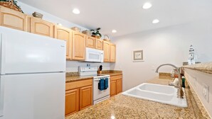 A kitchen with wooden cabinets, a white refrigerator, a microwave, a stove, and granite countertops. - 1313 - Paws in the sand, head in the sky (Westport)