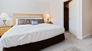 A neatly made bed with a wooden headboard, two bedside tables with lamps, and a door leading to a closet. - 1313 - Paws in the sand, head in the sky (Westport)
