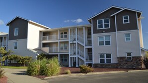 A multi-story apartment building with a central courtyard, balconies, and a stone foundation. - 1313 - Paws in the sand, head in the sky (Westport)