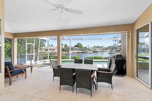 Eine Terrasse mit Tisch und Stühlen, einem Grill und Blick auf ein Gewässer und Häuser.