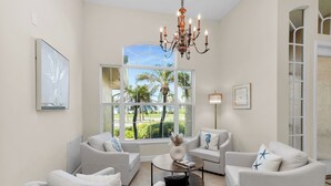 A spacious living room with white furniture, large windows, and a chandelier. - The Seahorse House I Wide Views on Tip Lot Minutes from the Gulf (Marco Island)