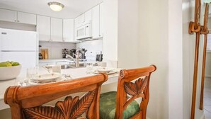 A modern kitchen with white cabinets, a dining table set with chairs, and a fruit bowl on the counter.