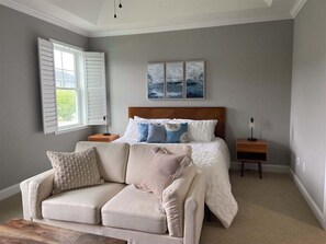 A bedroom with a bed, a sofa, a nightstand, and a wall-mounted painting.