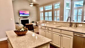 A kitchen with granite countertops, a built-in dishwasher, and a large window with blinds.