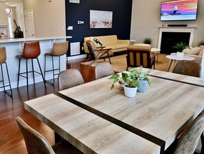 Ein modernes Wohnzimmer mit Esstisch, Barhocker, einer Couch und einem an der Wand montierten Fernseher.