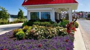 A white building with a red roof and a small tower, surrounded by a garden with various flowers.