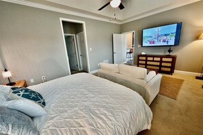 Ein Schlafzimmer mit einem Bett, einer Couch, einem Fernseher und einem Deckenventilator.