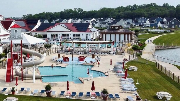 A resort with a large swimming pool, a water slide, and a covered area with lounge chairs and umbrellas.