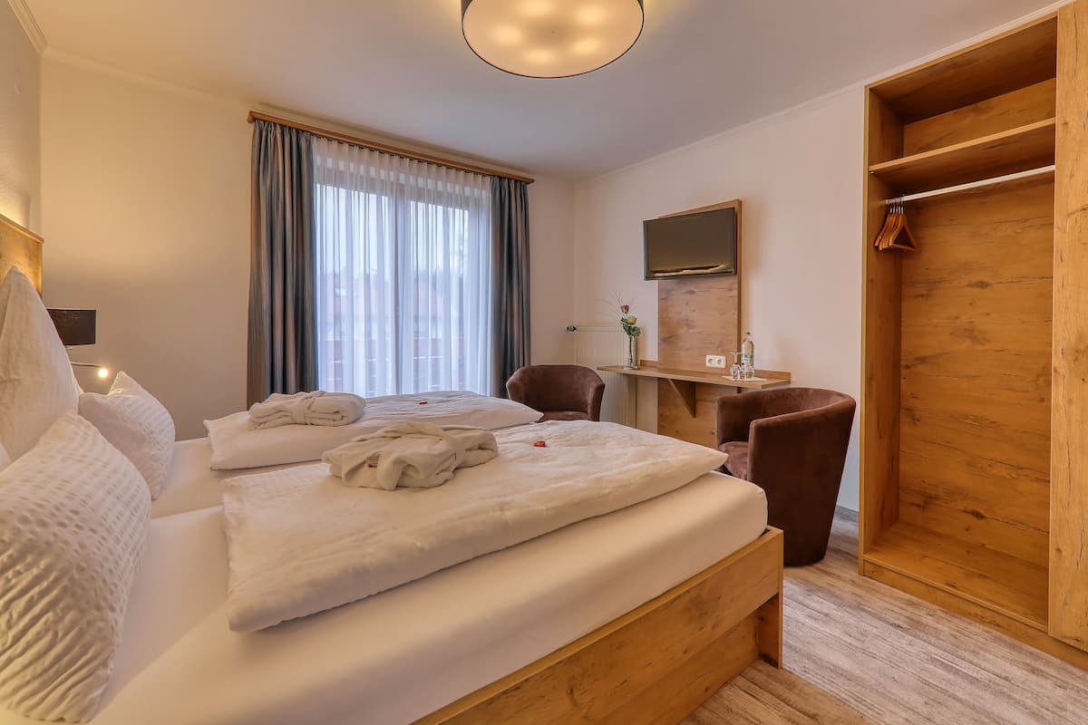 A hotel room with a bed, a desk, a chair, a wardrobe, and a window with curtains.