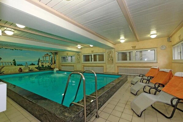 An indoor swimming pool with a mural, lounge chairs, and a clock on the wall. - Hotel Waldfrieden (Spiegelau)