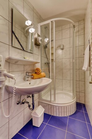 A bathroom with a white sink, a mirror, a shower enclosure, and a blue-tiled floor. - Hotel Waldfrieden (Spiegelau)