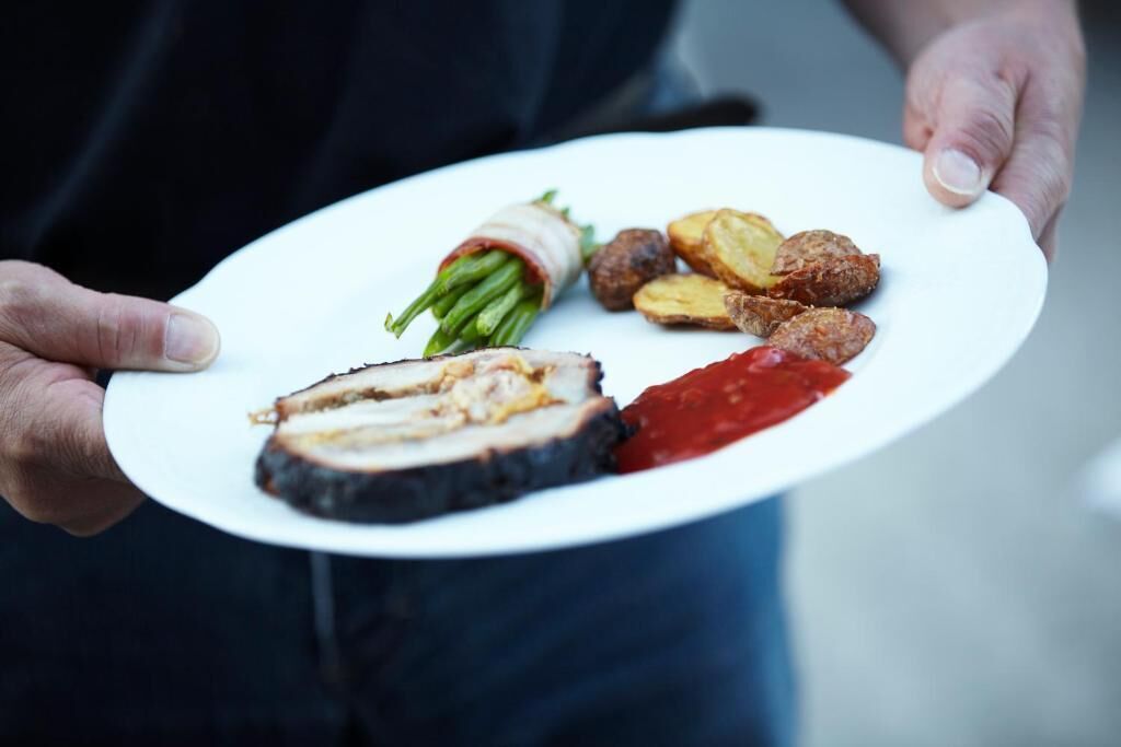 Eine Person hält einen Teller mit geschnittenem Fleisch, grünen Bohnen, Kartoffeln und roter Soße.