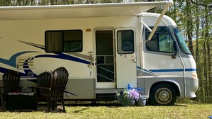 A recreational vehicle with a covered living area, a small table, two chairs, and a potted plant. - Cozy motorhome with loads of outdoor activities, farm animals and trails (Stockbridge)