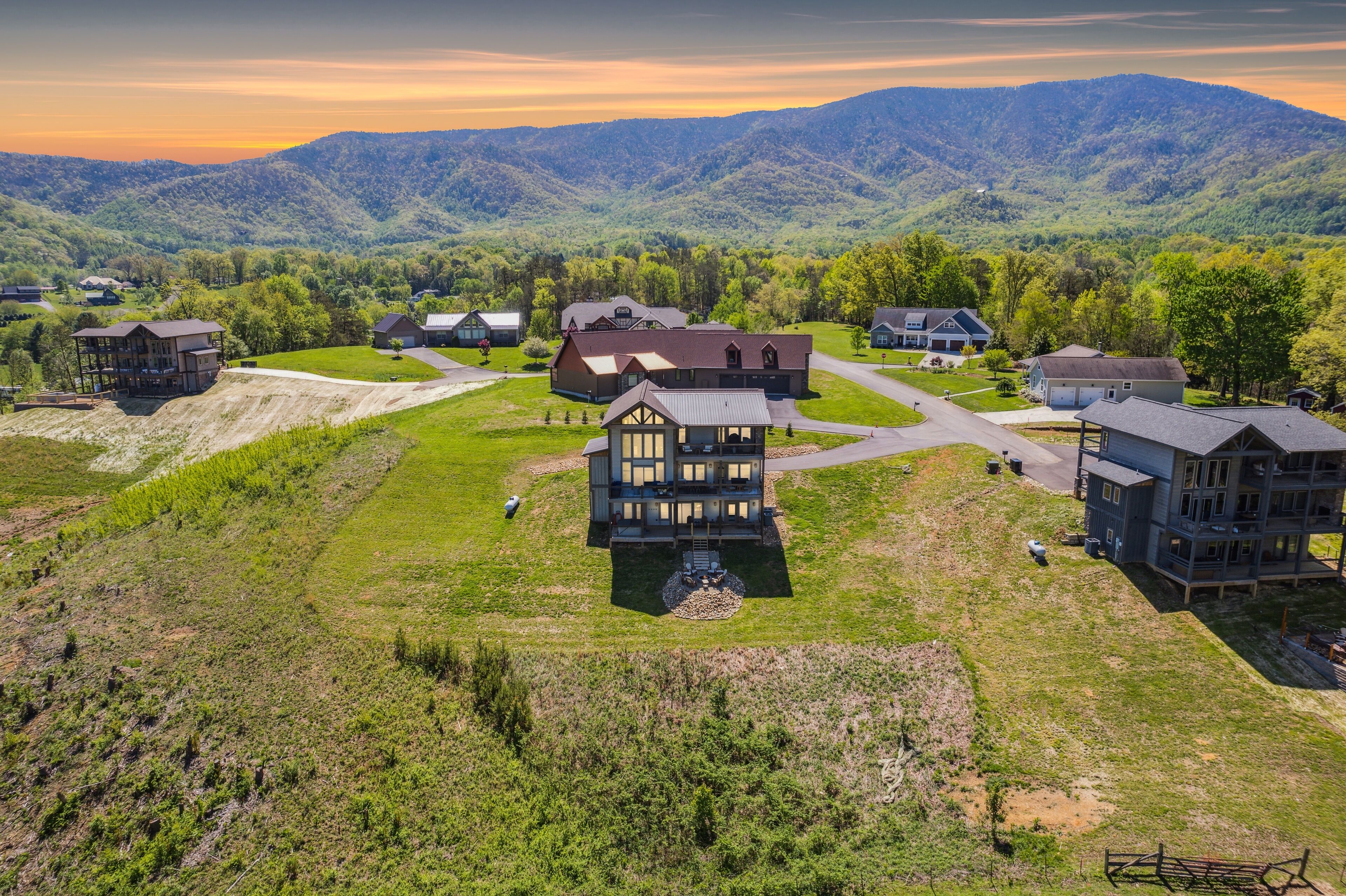 A residential area with multiple houses, a large central building, and a mountainous backdrop.