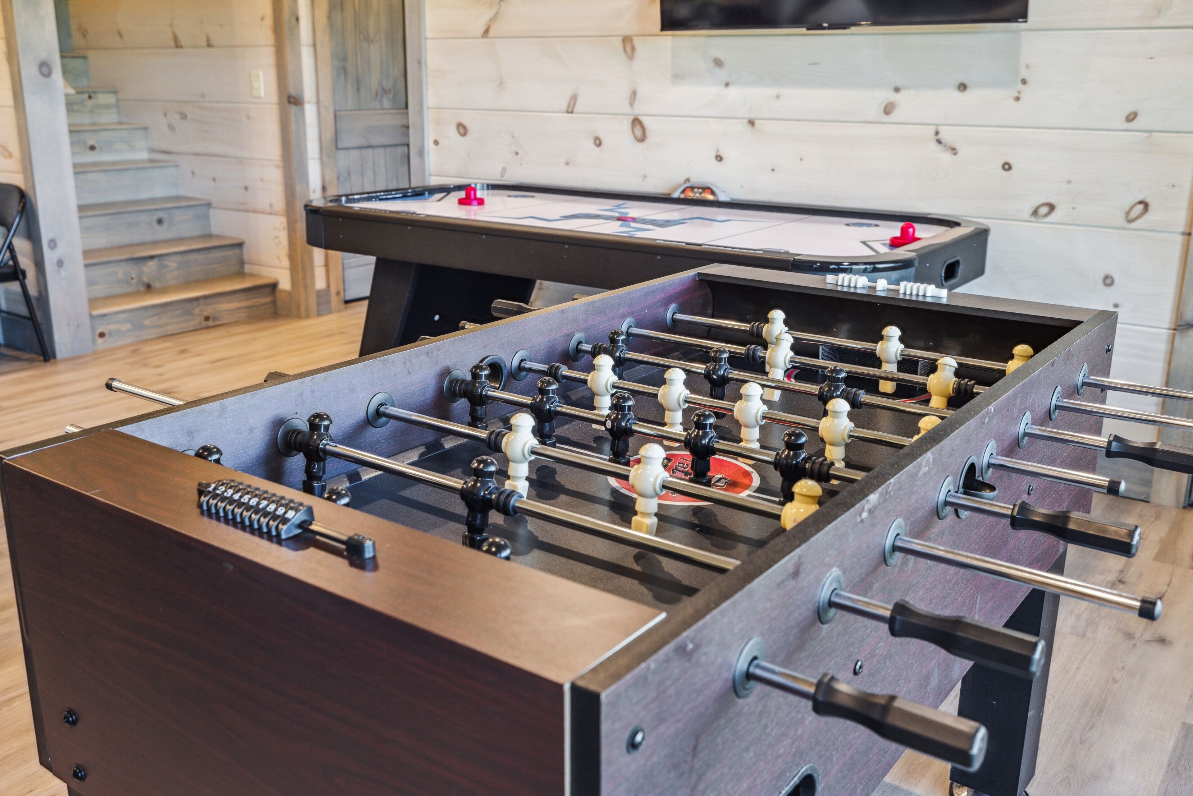 A foosball table in a room with wooden flooring and a staircase in the background.