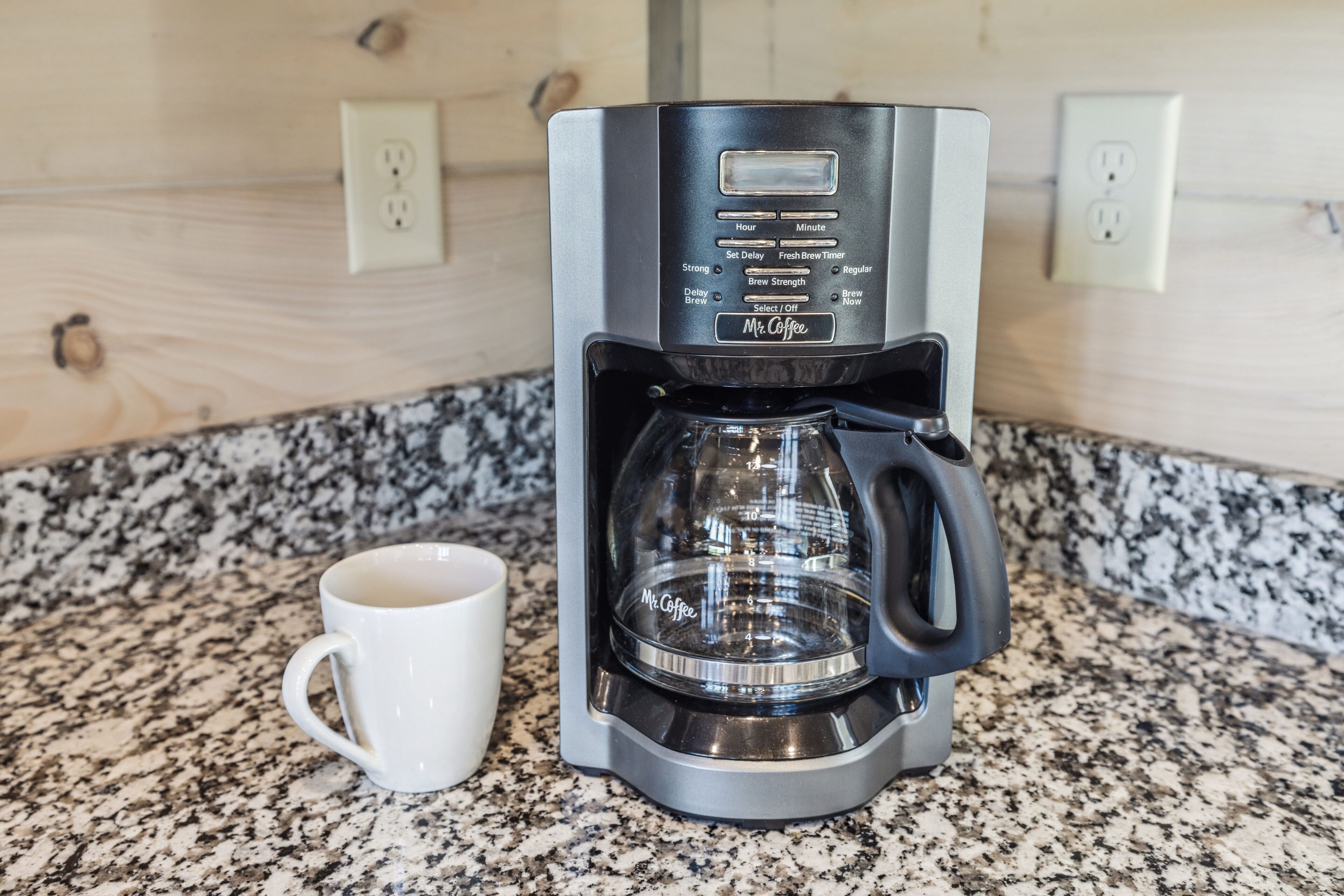 A coffee maker with a digital display and a cup on a granite countertop.
