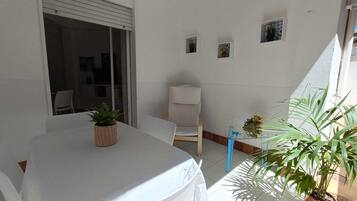 Ein kleines, sauberes Zimmer mit einem weißen Tisch und Stühlen, einer kleinen Topfpflanze und einem Fenster mit Blick.