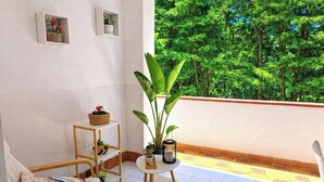 Un balcon donnant sur des arbres, une petite table avec une plante, une chaise et une étagère avec des objets décoratifs.