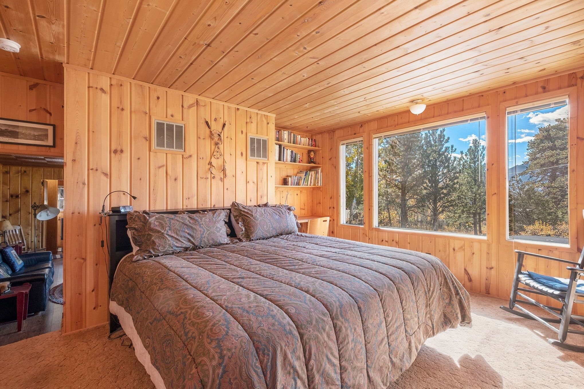 Camera da letto in una baita di legno, con un letto grande, scaffali e una poltrona a dondolo.